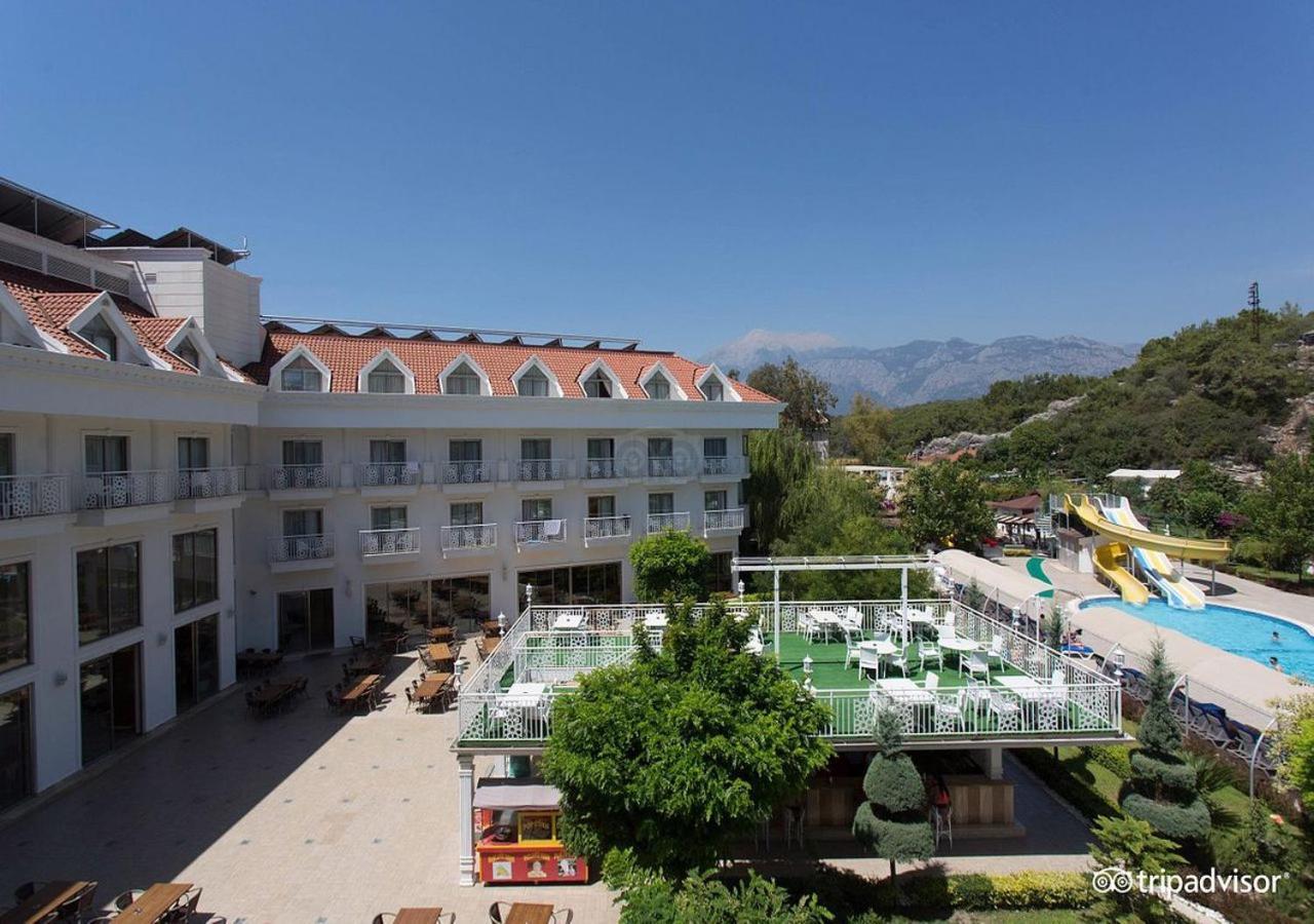 Miramor Hotel & Spa 安塔利亚 外观 照片 The photo shows a hotel or resort facility with a well-maintained exterior. There is a large green area with grass and some trees, likely intended for relaxation or recreational activities. In the background, there are water slides suggesting an amus